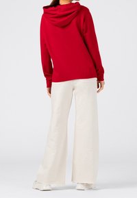 Czerwona bluza z kapturem o luźnym kroju. W połączeniu z białymi spodniami o szerokim kroju, które mają teksturowane wykończenie i postrzępiony dół.