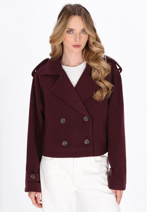 Burgunderfarbener doppelt geknöpfter Blazer mit großen Knöpfen, kürz design, breitem Kragen und Schulterriemen. Über einem weißen Oberteil getragen.