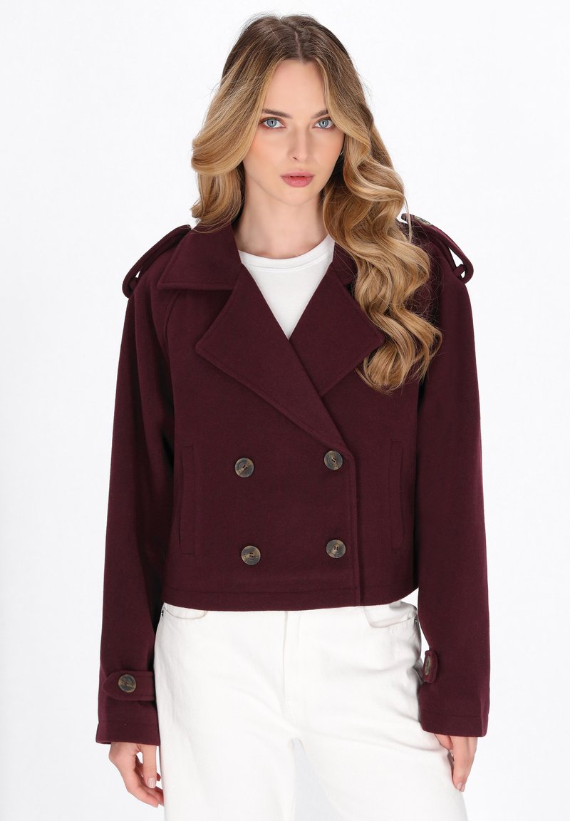 Jachetă burgundy cu două rânduri de nasturi, cu butoane mari, design scurt, guler larg și bretele. Purată peste un top alb.