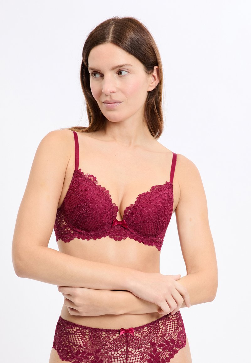 Bordowy koronkowy biustonosz z usztywnianymi miseczkami, regulowanymi ramiączkami i kwiatowym wzorem. Posiada kokardkę na środku dla dodatkowego akcentu.