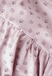Tissu rose clair présentant un motif de petites coquillages violets foncés et de points, avec une texture froncée le long du bord inférieur.
