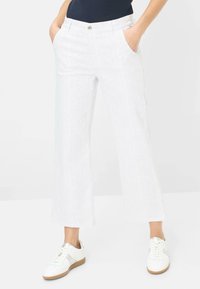 Pantaloni larghi a righe bianche con tasche laterali e chiusura frontale con bottone, abbinati a sneaker bianche con un accento argento.