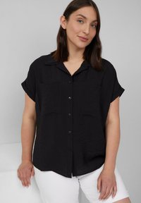 Zwarte kortpolkshirt met knopen en twee borstzakken, met een gestructureerde afwerking; gecombineerd met witte shorts.