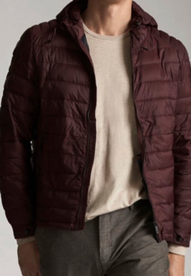 Bordeaux farvet quilted jakke med hætte, har en frontlynlås, holdbart materiale og sidelommer. Bæres over en lys beige skjorte.