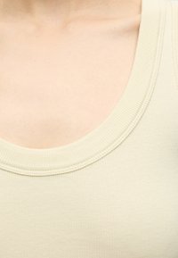 Gros plan du cou et de la partie supérieure de la poitrine portant un débardeur en tissu côtelé beige clair avec un col rond.