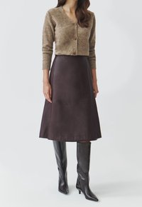 Cardigan in misto lana marrone con scollo a V e cinque bottoni, abbinato a una gonna A-line in pelle marrone scuro e stivali marroni al ginocchio.