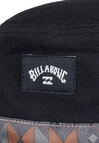 Svart stoff med et synlig Billabong-logo-patch. Under er det et mønsterdesign i grått og oransje som fremhever kanten.