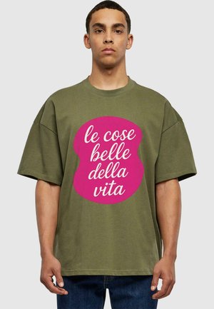 Olivgrünes, übergroßes T-Shirt mit einem runden, pinken Grafik, das weißen Text enthält. Kurze Ärmel, Baumwollmaterial, lässige Passform.