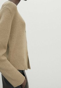 Beige knitted sweater with a round neckline, long sleeves, and side slits. Textured fabric offers a soft appearance and relaxed fit.