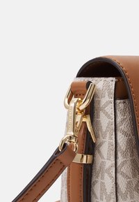 Close-up of tan and beige designer handbag strap with gold clasp and branded hardware details.