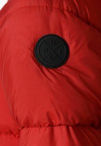 Röd puffjacka i tyg med slät textur, med en svart cirkulär patch märkt "NMT 97" på överarmsområdet.