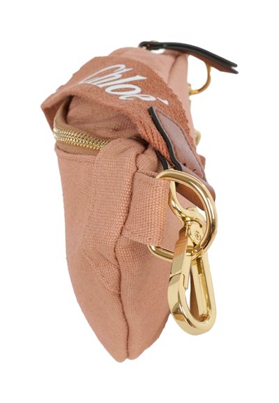 Sac en toile rose tendre avec fermeture éclair et quincaillerie dorées, doté d'une bandoulière en cuir marron avec détail de logo. Design compact et rectangulaire.
