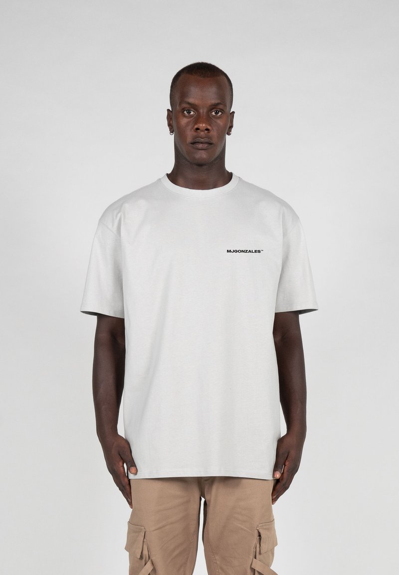Light grey cotton t-shirt with a relaxed fit, short sleeves, and a logo printed in black on the left chest. Plain design, soft texture.