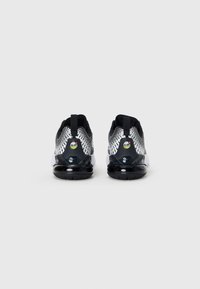 Sapatilhas em preto e branco com um upper texturizado, design padrão e uma unidade de ar visível. Apresentam uma sola preta e uma alça de puxar.