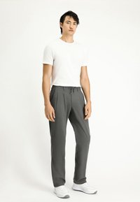 Pantaloni grigi su misura con frontale plissettato e coulisse regolabile, abbinati a una t-shirt attillata bianca e sneaker bianche.