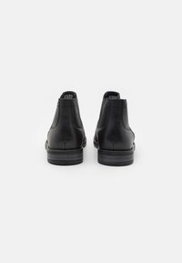 Botas de tobillo de cuero negro con una textura suave, punta redondeada y tacón apilado, con paneles laterales elásticos para una fácil colocación.