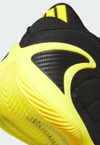Gros plan sur le talon d'une chaussure de sport noire et jaune vif avec une semelle texturée et trois rayures jaunes sur la tige noire.