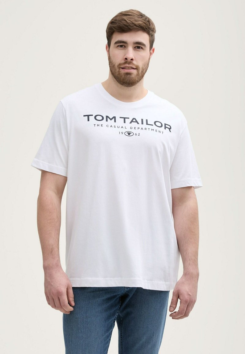 Camiseta de algodón blanca con cuello redondo, mangas cortas y un logotipo impreso "TOM TAILOR" en letras negras en negrita a lo largo del pecho.