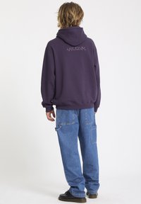 Purple hoodie with a large hood, featuring a graphic on the back. Paired with blue denim cargo pants and black shoes.