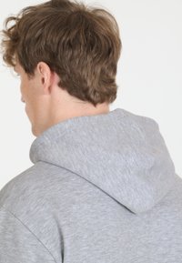 Harmaa huppari pehmeästä, harjatusta kankaasta. Siinä on rento leikkaus ja näkyvät ompeluyksityiskohdat saumoissa.