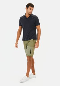 Marineblaues Polohemd mit kurzen Ärmeln und Brusttasche, kombiniert mit olivgrünen Cargo-Shorts mit seitlichen Taschen und schwarzen Reißverschlüssen, getragen mit weißen Sneakers.