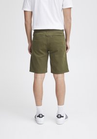 Olivgröna shorts i bomull med rak passform, knälång klippning, elastisk midja och två bakfickor. Bärs med vita sneakers.