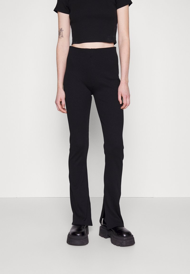 Zwarte aansluitende cropped top gecombineerd met zwarte flared broek met slits aan de manchetten, gemaakt van een zachte textuurstof. Chunky zwarte schoenen.