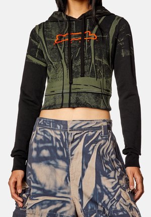Kobieta nosząca krótki czarno-zielony kaptur z pomarańczowym detalem oraz luźne spodnie z wysokim stanem z niebiesko-beżowym wzorem tie-dye.