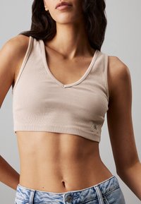 Top corto beige de canalé con escote en V y dobladillo cosido, que presenta una pequeña etiqueta de logo. Combinado con shorts de mezclilla de tiro alto en azul claro.