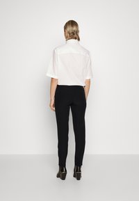 Vit kortärmad skjorta med spetsig krage, i kombination med svarta skräddarsydda byxor och glänsande svarta ankelskor. Enkel design och rena linjer.