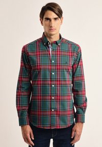 Camisa de botones de cuadros en verde y rojo. Presenta un cuello tipo polo, mangas largas y botones blancos. Tejido suave con un corte estructurado.