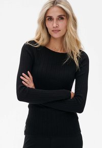 Schwarzer gerippter Langarmpullover mit Bootsausschnitt und strukturiertem Stoff. Figurbetonte Silhouette mit seitlichen Schlitzen am Saum.