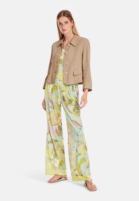 Beige linen jacket with large buttons paired with a floral-patterned light blue top and wide-leg pants in pastel colors. Flat sandals.