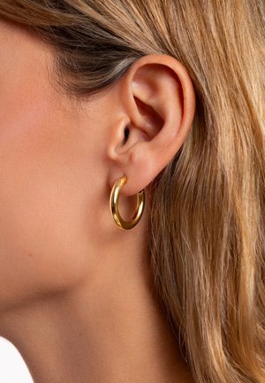 Goldfarbene Creolen mit einer glatten, glänzenden Oberfläche, großem, rundem Design und einer Dicke, die einen eleganten, modernen Look erzeugt.