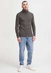 Grijze gebreide coltrui met geribde manchetten en zoom, gedragen met lichtblauwe jeans en witte sneakers. Heeft een textuurafwerking.