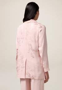 Blush roze satijnen jas met een subtiel bloemenpatroon, lange mouwen en een geknipt kraag. Beschikt over een centrale naad en een ontspannen fit.