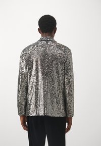 Blazer d'argento con design strutturato. Presenta un colletto a punta e maniche lunghe, mettendo in mostra una superficie lucida e testurizzata.
