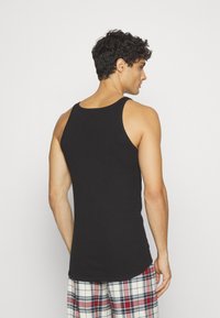 Débardeur en coton noir avec un col rond, sans manches et une texture lisse, associé à un pantalon de pyjama à carreaux.