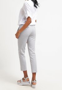 Biała lniana koszula z podwiniętymi rękawami, wzorzyste szare spodnie w kratę oraz szare sandały na platformie. Widok z tyłu, krótka długość z dopasowanym krojem.