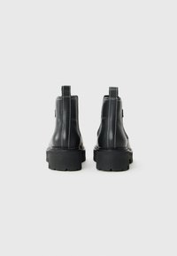 Bottes de cheville en cuir noir avec une semelle épaisse, des coutures blanches et des passants à l'arrière. Tige texturée, construction robuste.