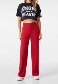 Rode wijde broek met hoge taille en knoopsluiting, gecombineerd met een cropped marineblauw T-shirt met grafische opdruk en dikke witte letters.