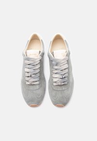 Ζευγάρι γκρι σουέντ αθλητικών παπουτσιών με μπεζ εσωτερικό, λευκές ετικέτες στη γλώσσα και γκρι κορδόνια με μικρά ασημένια διακοσμητικά.