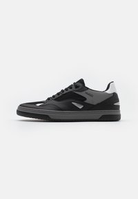 Baskets de sport noires avec un mélange de mailles et de cuir synthétique, présentant un profil bas, un bout rond et des accents gris. Lacets et logo visibles.