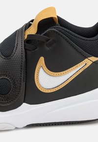 Musta urheilukenkä, jossa on teksturoitu nahkainen yläosa, pehmustettu nilkkaosa, verkkokohdat ja kontrastivärinen kultainen swoosh-muotoilu. Valkoinen pohja.