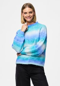 Light blue and teal gradient sweater with ribbed cuffs and neckline, featuring a soft, textured knit. Paired with dark pants.