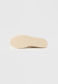 Μπεζ λαστιχένια σόλα παπουτσιού με υφή πέλματος και λεπτομέρειες λογότυπου. Διαθέτει ελαφρώς ανυψωμένες κουκκίδες για καλύτερη πρόσφυση και λεία περίμετρο.