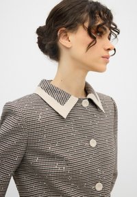 Blazer a quadri in tessuto beige e marrone, con colletto a contrasto, chiusura con bottoni e sottili dettagli in paillettes. Design strutturato.