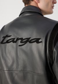 Zwarte leren jas met een soepele textuur en hoge kraag, versierd met een prominent zwart geborduurd "targa"-logo op de achterkant.