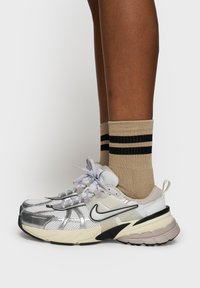 Nike sneakers med en reflekterende sølvnetoverdel, beige accenter, sorte detaljer og en tyk hvid og sort sål, parret med beige sokker med sorte striber.