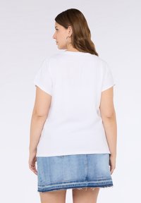 Camiseta blanca de manga corta con escote redondo, combinada con una falda de mezclilla azul con dobladillo deshilachado y costuras decorativas.